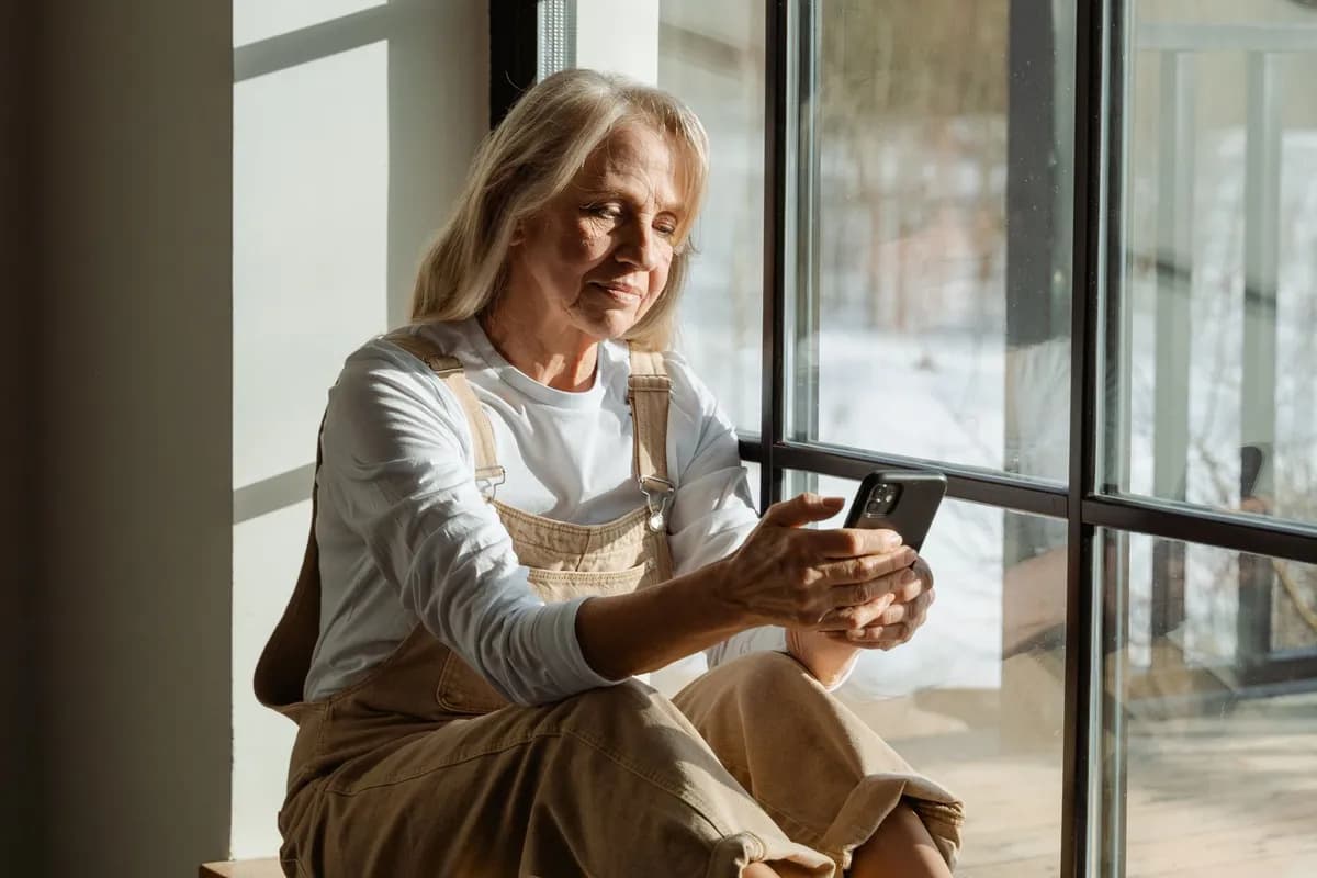 A grandmother sitting by a window, looking at photos on her phone